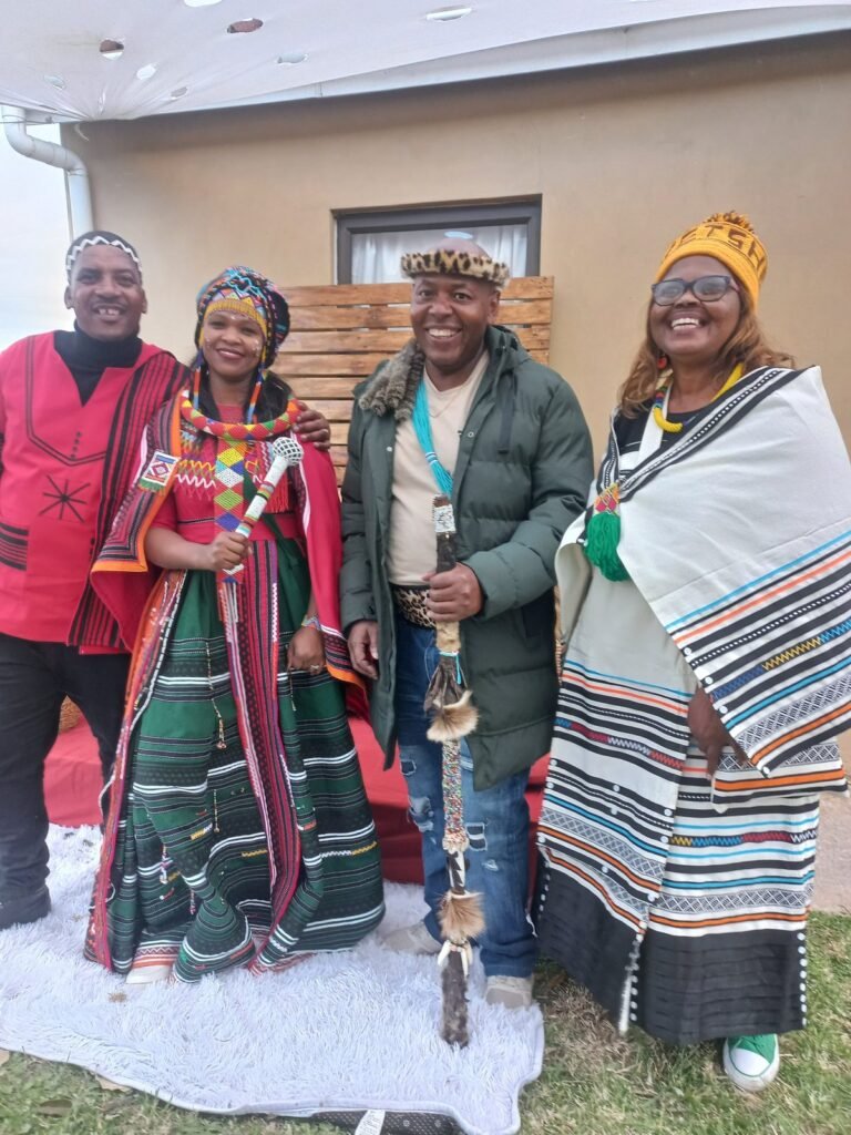 Four people in colourful traditional attire and beadwork posing together at an outdoor celebration
